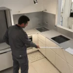 Artisan mesurant l'implantation d'une petite cuisine de 4 m² en configuration en L lors de travaux de rénovation dans un appartement parisien.