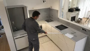 Artisan mesurant l'implantation d'une petite cuisine de 4 m² en configuration en L lors de travaux de rénovation dans un appartement parisien.