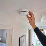 Installation d’un détecteur de fumée DAAF au plafond d’un couloir dans un logement résidentiel français, avec une main en train de fixer l’appareil conformément aux obligations de sécurité incendie.
