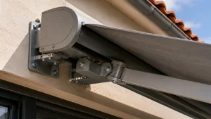 Quelle fixation choisir pour un store banne selon la nature du mur Gros plan sur les supports de fixation murale d'un store banne coffre déployé, solidement ancrés sur une façade extérieure en enduit.
