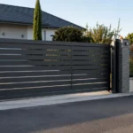 Portail coulissant autoportant en aluminium installé à l'entrée d'une maison, avec vantail suspendu sans rail au sol, poteau de réception visible et allée dégagée.