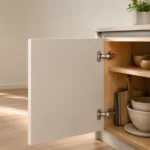 Porte de meuble de cuisine entrouverte avec charnières invisibles fixées sur le caisson en bois clair.