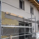 Façade de maison en rénovation avec isolation thermique par l’extérieur et fixation pour charge lourde destinée à un auvent métallique.