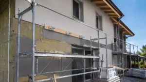 Façade de maison en rénovation avec isolation thermique par l’extérieur et fixation pour charge lourde destinée à un auvent métallique.