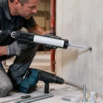 Artisan injectant une résine de scellement chimique dans un trou percé dans un mur en béton avant la pose d’une tige filetée.
